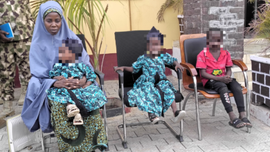 Woman in blue hijab sitting next to children in matching outfits, faces pixelated for privacy.