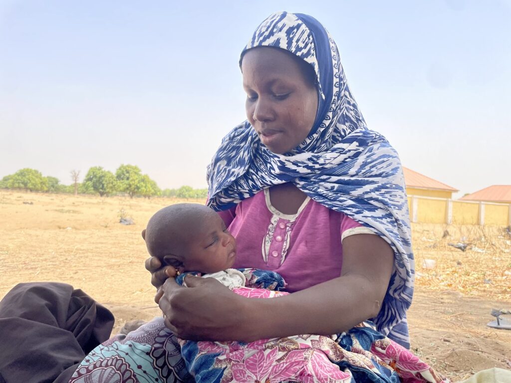 A mother in traditional attire lovingly holding her sleeping baby outdoors.