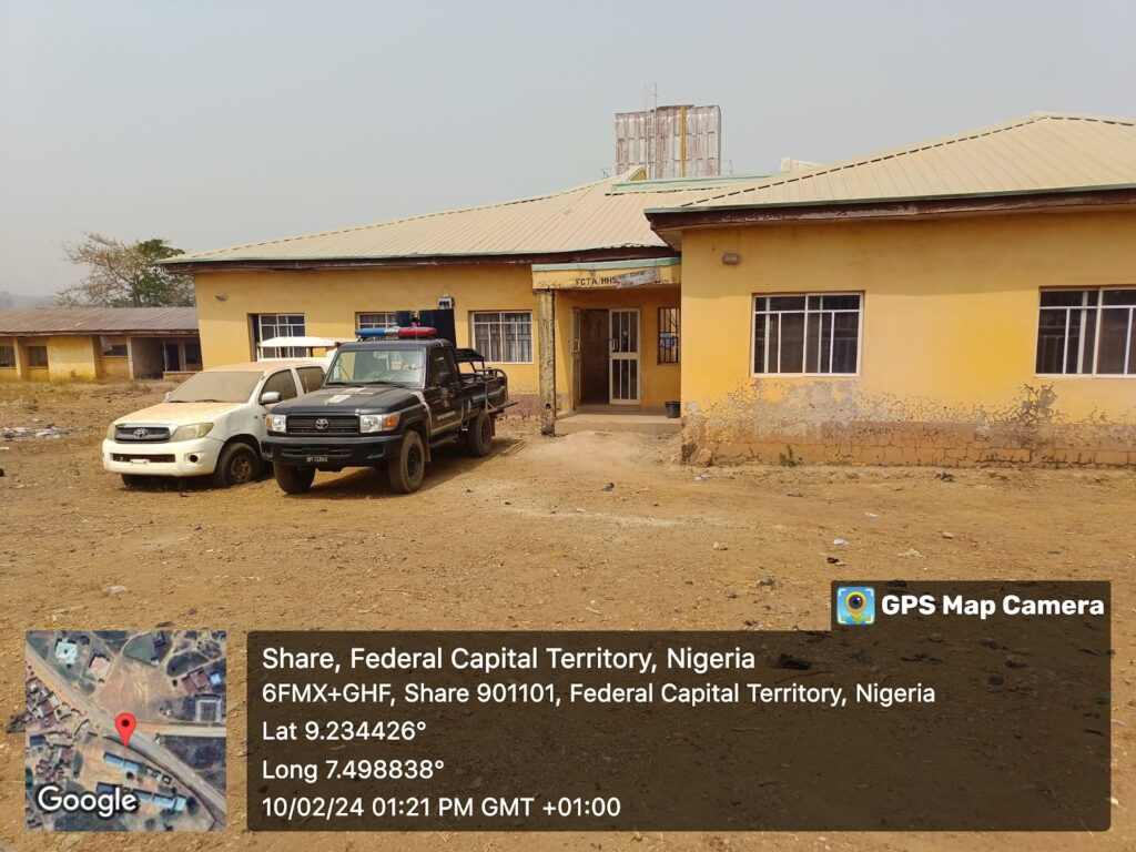 Two pickup trucks parked outside a yellow building with GPS coordinates overlay in Nigeria.