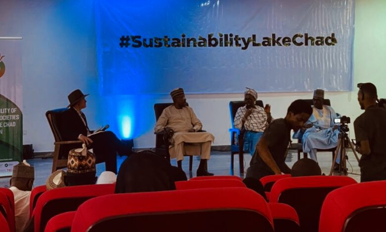 Panel discussion in progress under a #SustainabilityLakeChad banner with attendees and camera crew present.