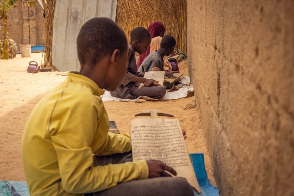 Children studying with traditional wooden slates beside a mud wall.