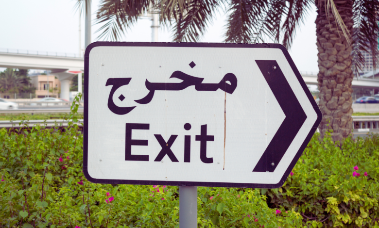 "Exit sign in English and Arabic with an arrow, surrounded by greenery and a palm tree in the background."