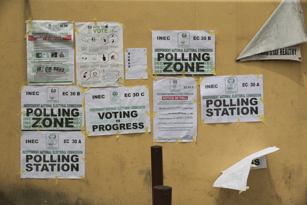 A wall with various election-related posters and a torn white sheet, indicating an active polling station area.