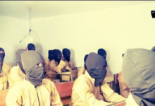 Students in a classroom with heads covered by cloth, sitting at wooden desks.