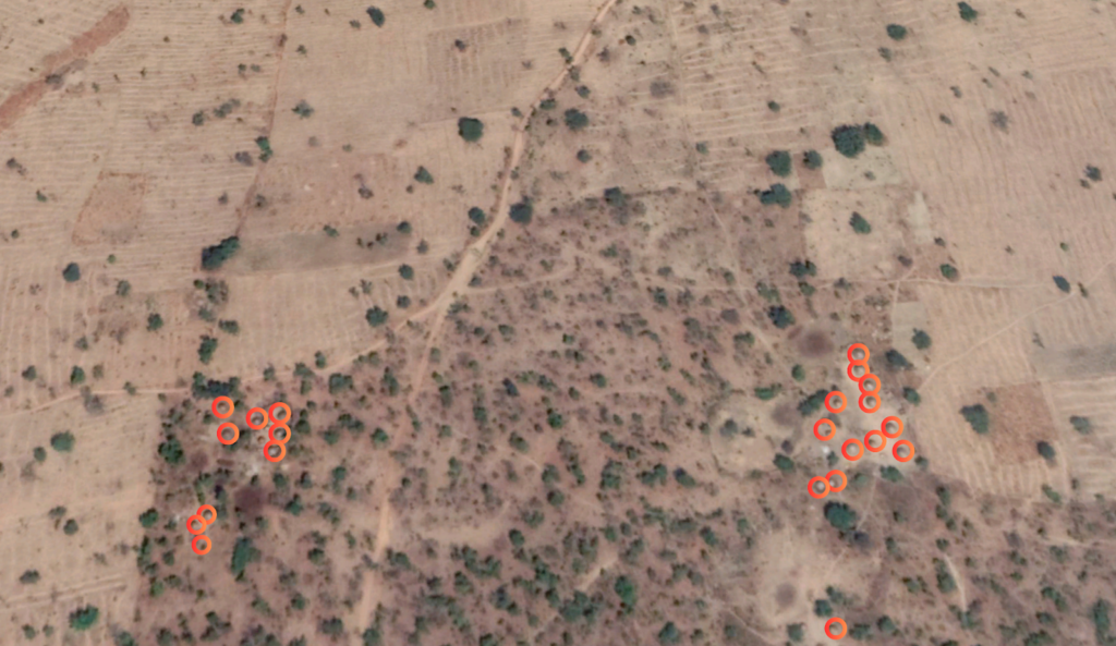 Aerial view of a dry landscape with sparse vegetation and scattered red circles indicating specific points of interest.