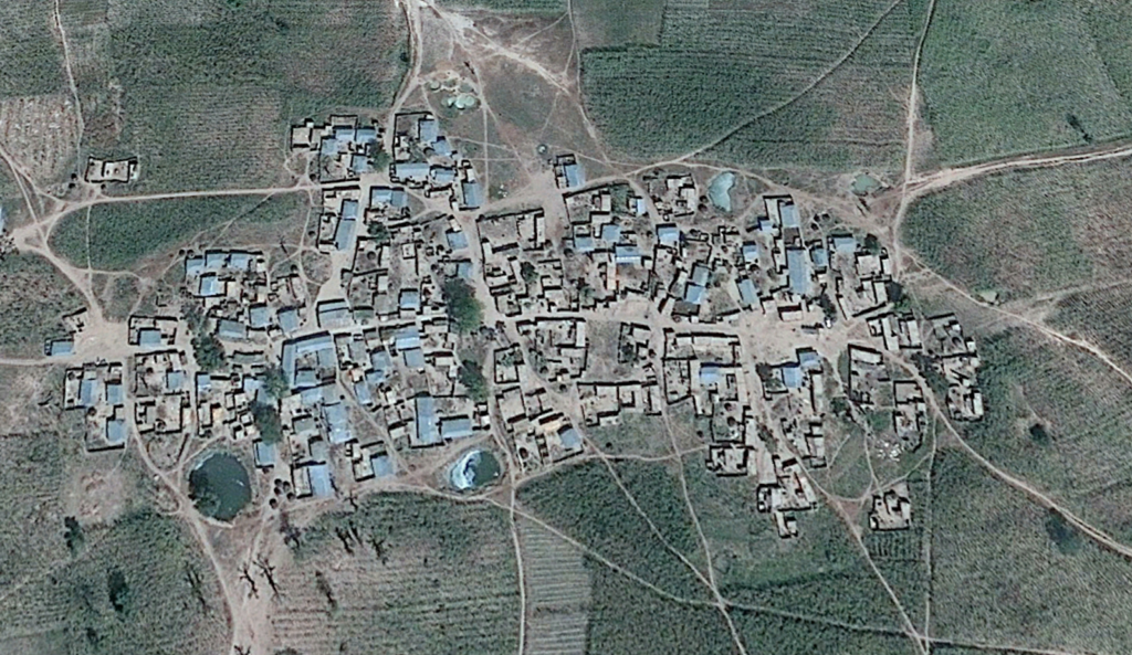 Aerial view of a clustered village with irregular building patterns surrounded by fields.