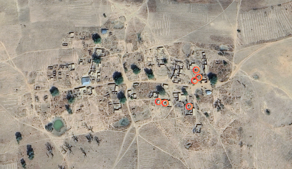 Aerial view of a rural area with scattered buildings and patches of vegetation, marked by red circles.