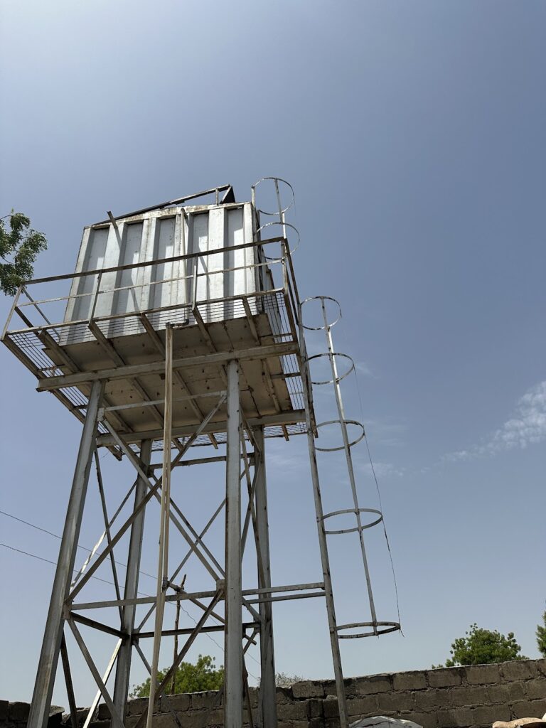 Elevated metal water tower with a spiral staircase against a clear blue sky.