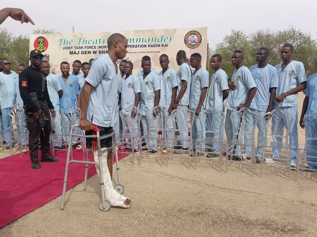 A group of individuals in blue uniforms standing behind metal chairs with a person on crutches in the foreground.