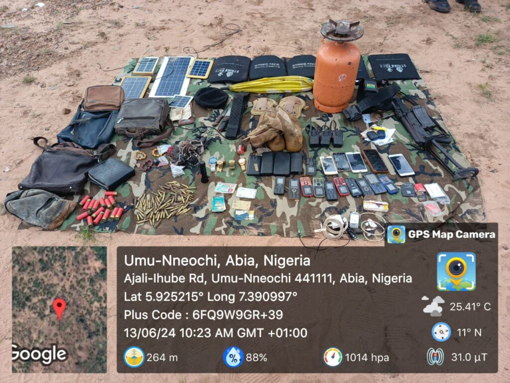 Assorted items including bags, ammunition, phones, and firearms spread on a camouflage mat, with GPS data overlay.