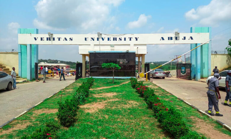 Entrance gate of Veritas University Abuja with people and cars nearby.