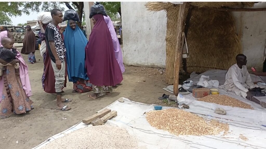 People conversing in a market area with grain spread out on the ground for drying.