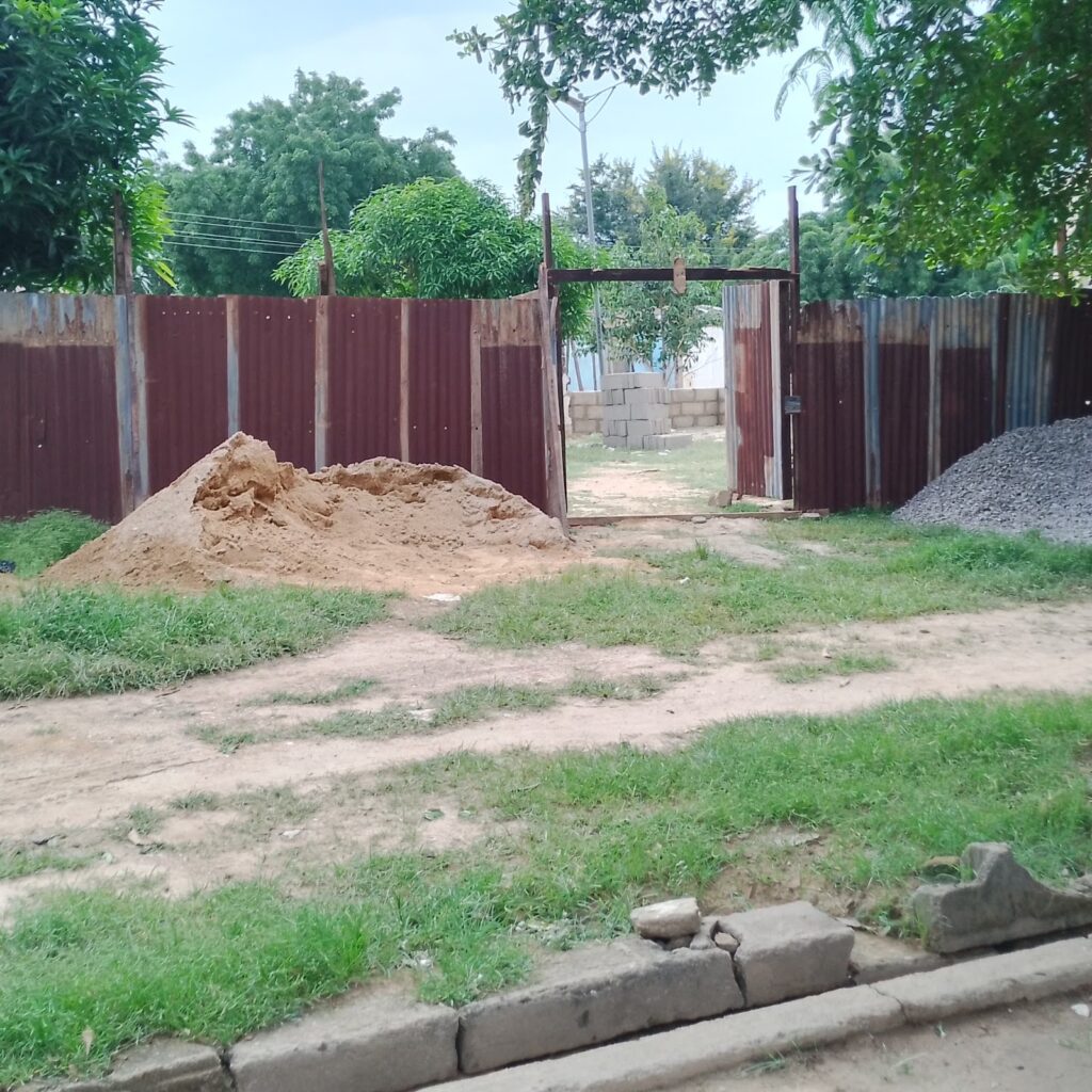 Rustic construction site with piles of sand and gravel, metal gate, and green trees.