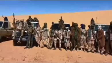 A group of people in desert attire posing in front of vehicles on a sandy terrain.