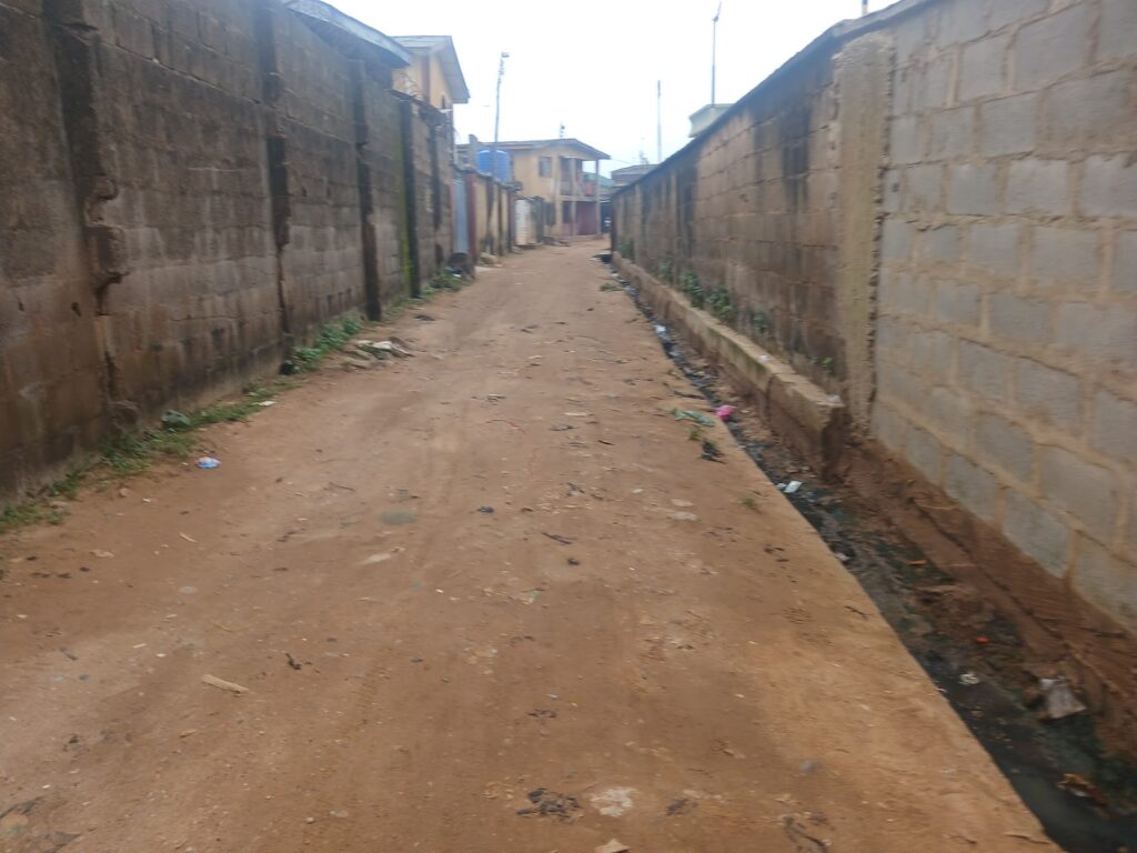 A dirt road flanked by high concrete walls with scattered litter.