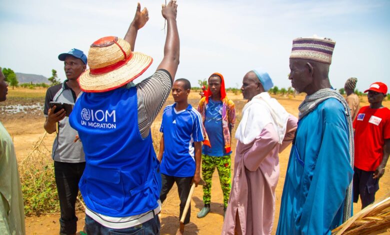 Group of people with a person in a blue UN Migration vest interacting with locals in a rural setting.