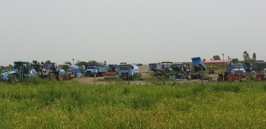 A collection of various blue agricultural machinery and trucks parked in a green field.