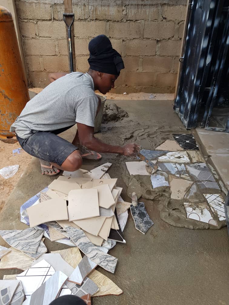 Person laying tiles outdoors with trowel and various tiles scattered around.