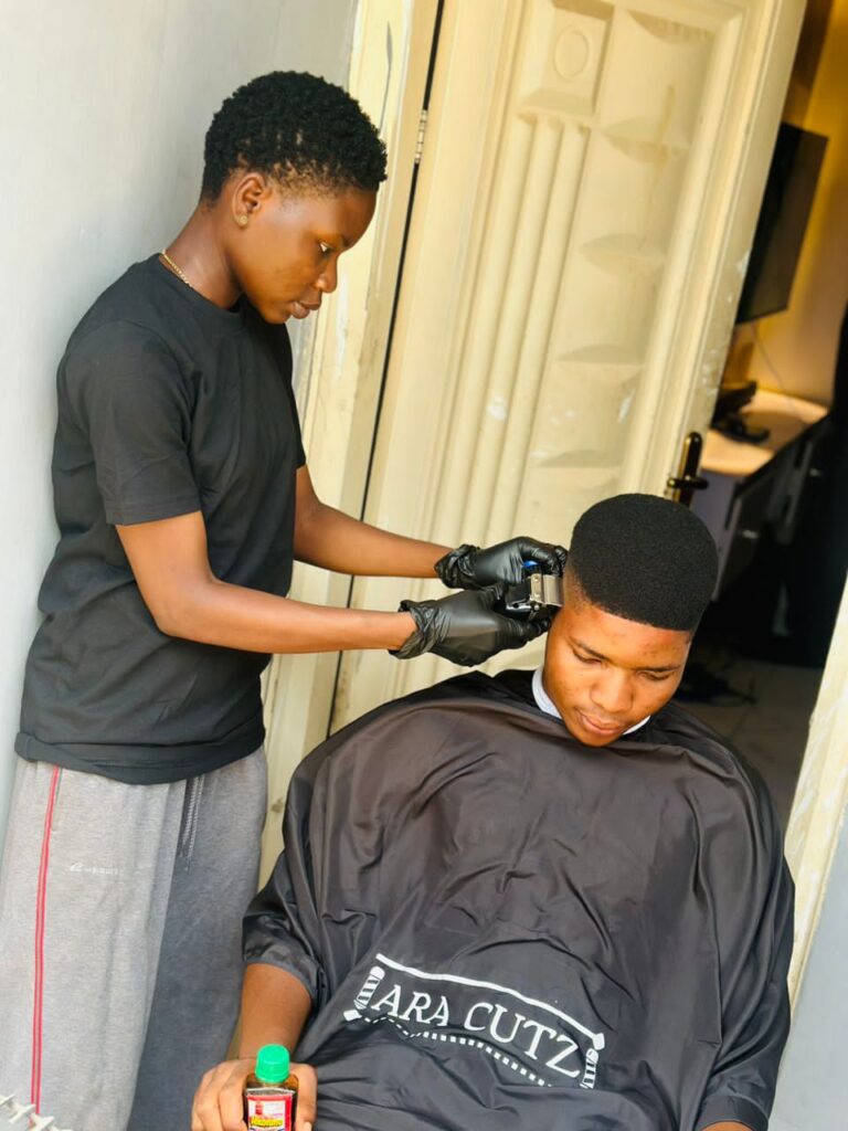 A barber in black gloves giving a haircut to a client wearing a salon cape.