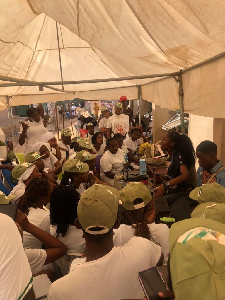 Group of people in white and green attire sitting under a tent, engaged in conversation.