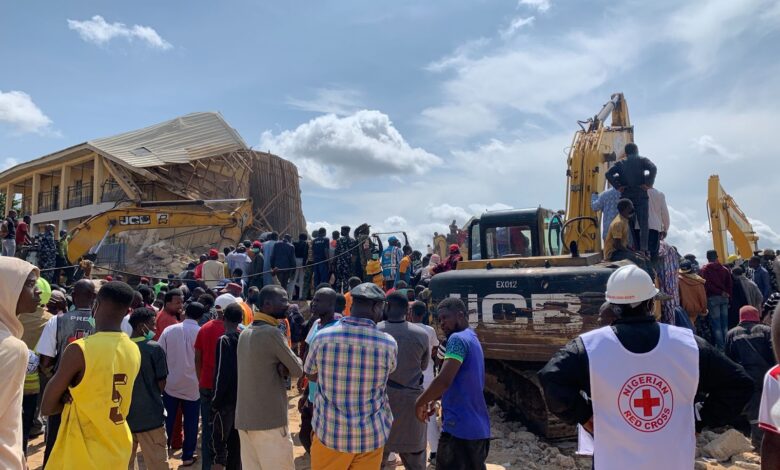 Crowd and emergency responders around a collapsed building with excavators at work.