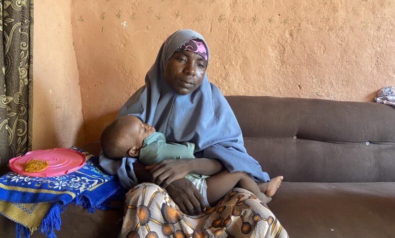 Woman in a headscarf holding a sleeping child on a sofa, with a colorful plate beside her.