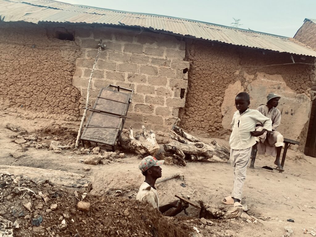 Children and a man by a mudbrick house with a metal roof in a rural setting.