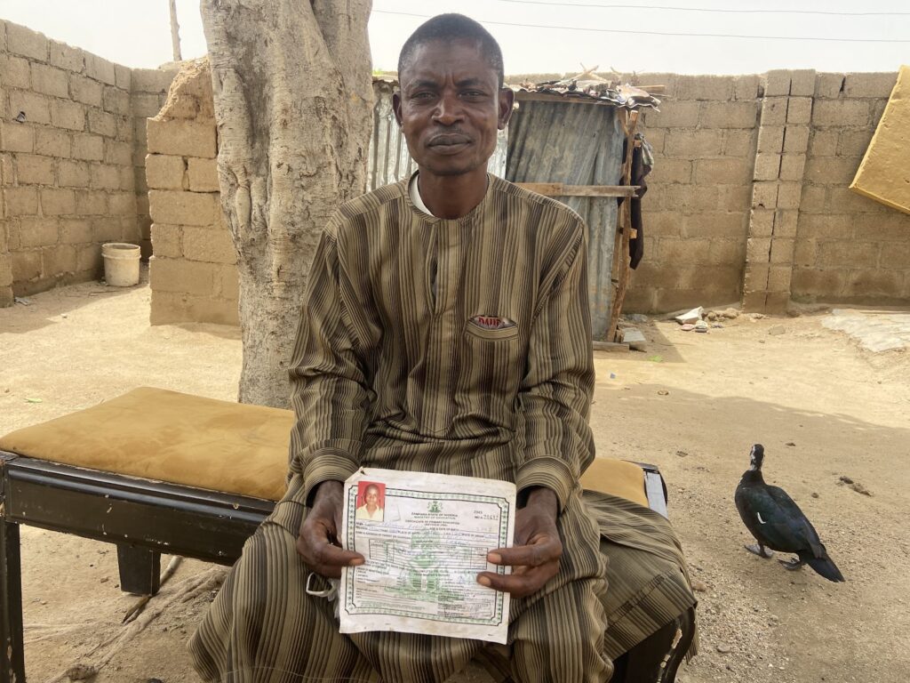 Man in striped attire sitting outdoors, holding a document, with a pigeon nearby.