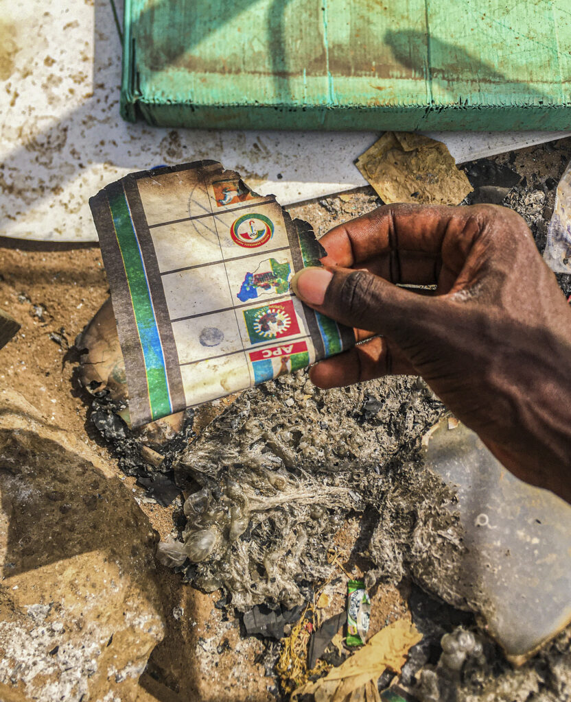 Hand holding a charred document among debris and ashes.