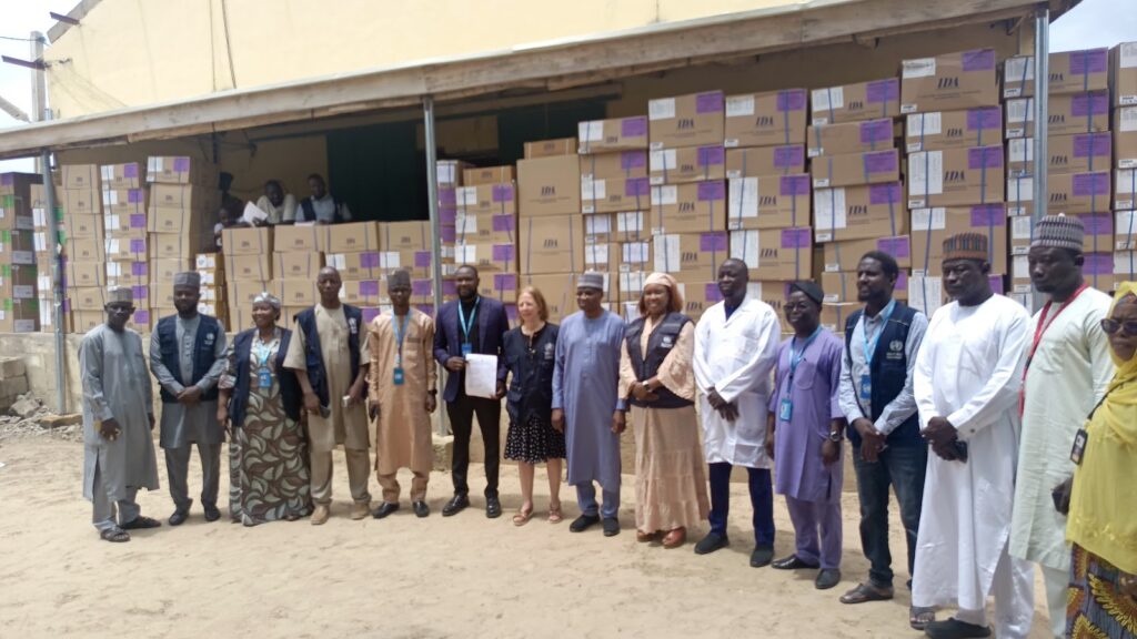 Group of people standing in front of a warehouse with stacks of boxed supplies.