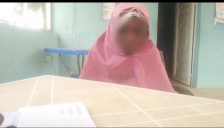 A person wearing a pink hijab sitting at a table, with their face blurred for privacy.