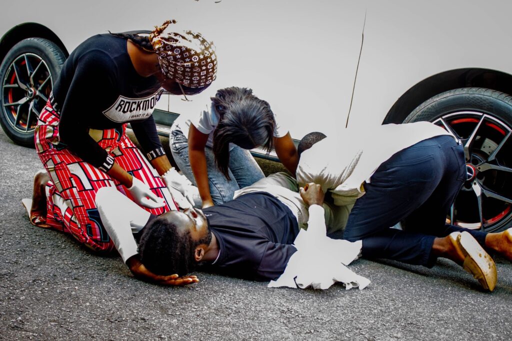 Three people attending to a man lying on the ground by a car.