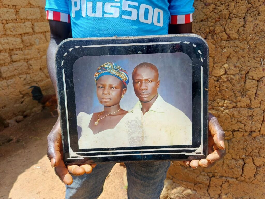 Person holding a worn framed photo of a man and woman against an earthy background.