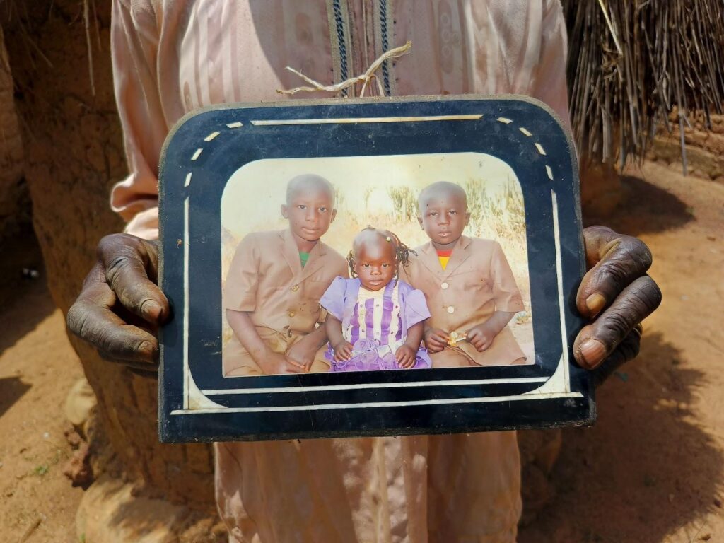 Hands holding a framed photograph of three children outdoors.