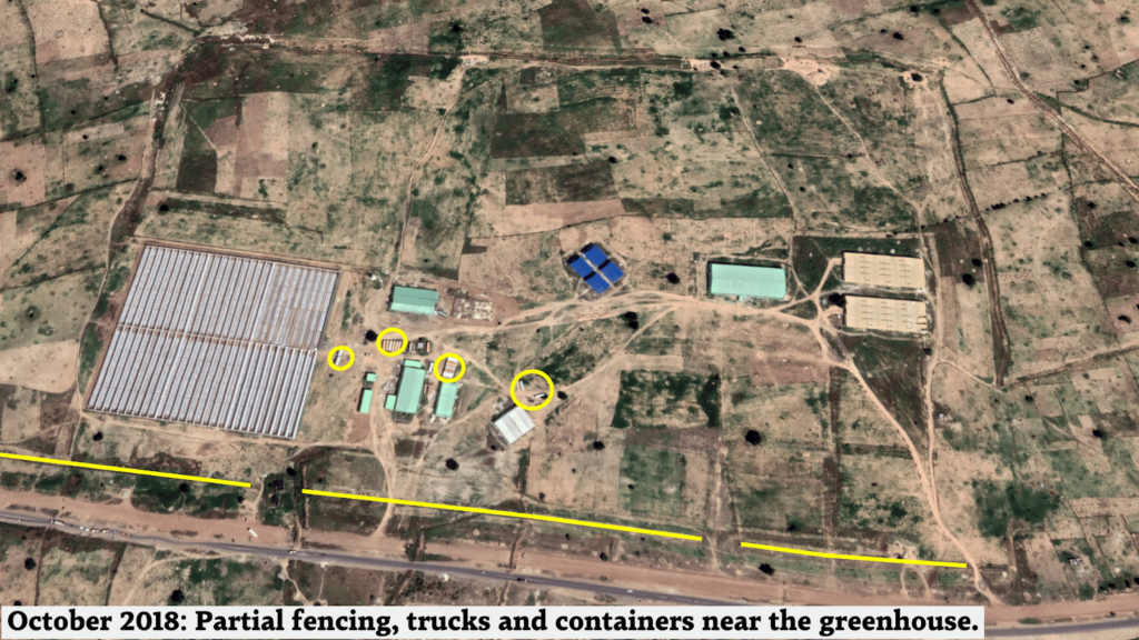 Aerial view of a rural area with annotated features such as partial fencing, trucks, and containers near a greenhouse.