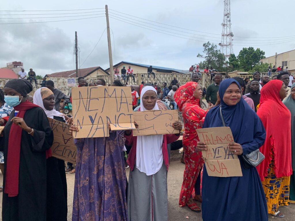 A group of women holding protest signs on a street with onlookers in the background.