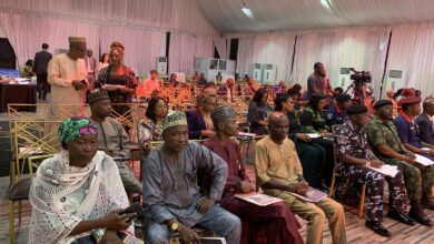 Attendees seated in a conference hall, some in traditional attire, with a videographer recording the event.