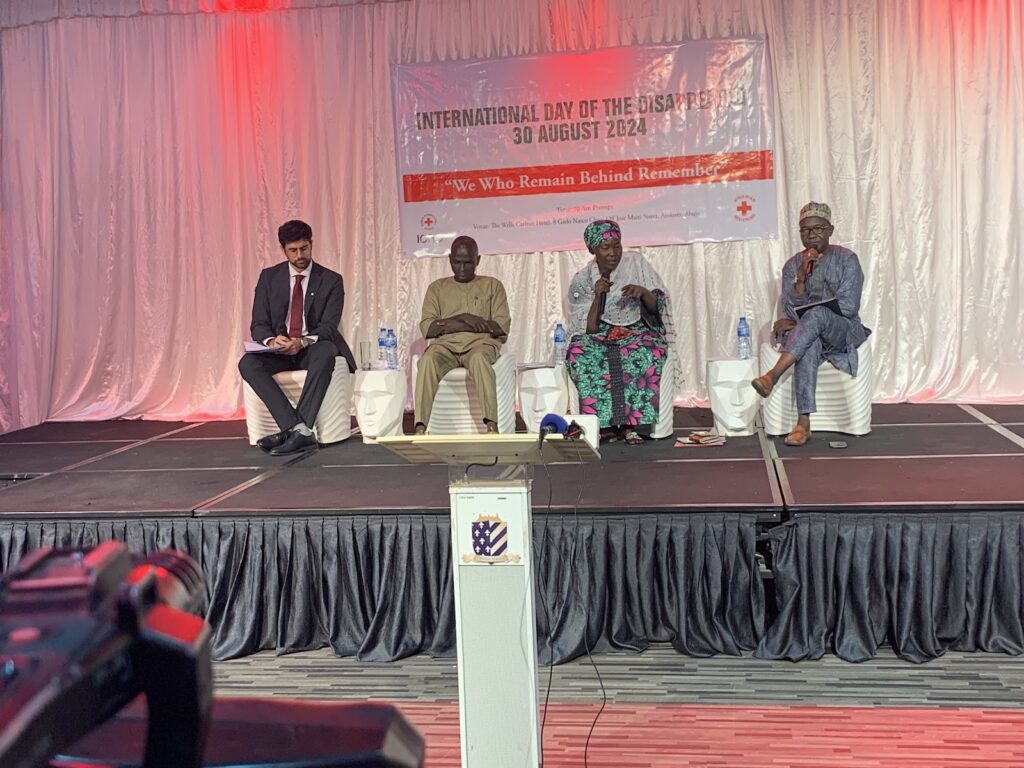 Four panelists sitting on stage under a banner for "International Day of the Disappeared" event.