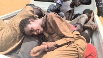 Several people lying in the back of a pickup truck, with a focus on one individual looking at the camera.