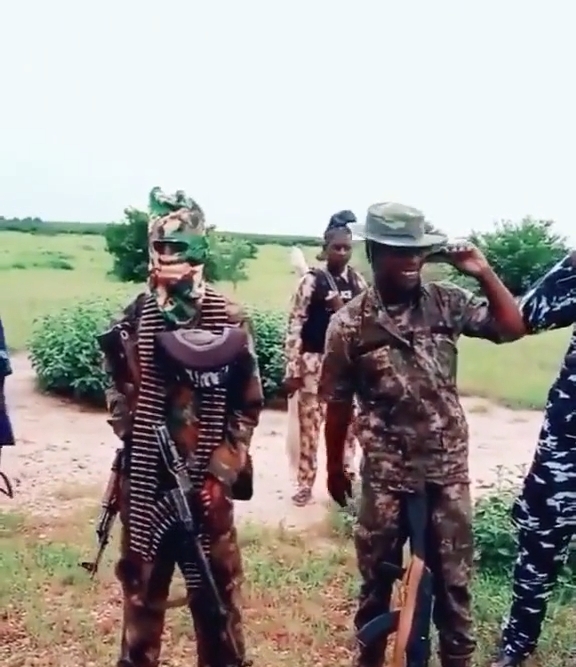 Three individuals in military camouflage with one saluting and another in face paint.