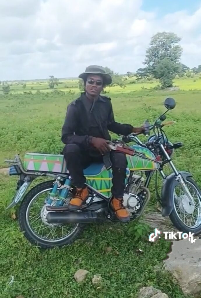 Person in black attire and hat sitting on a motorcycle with patterned saddlebags, TikTok logo visible, outdoors.