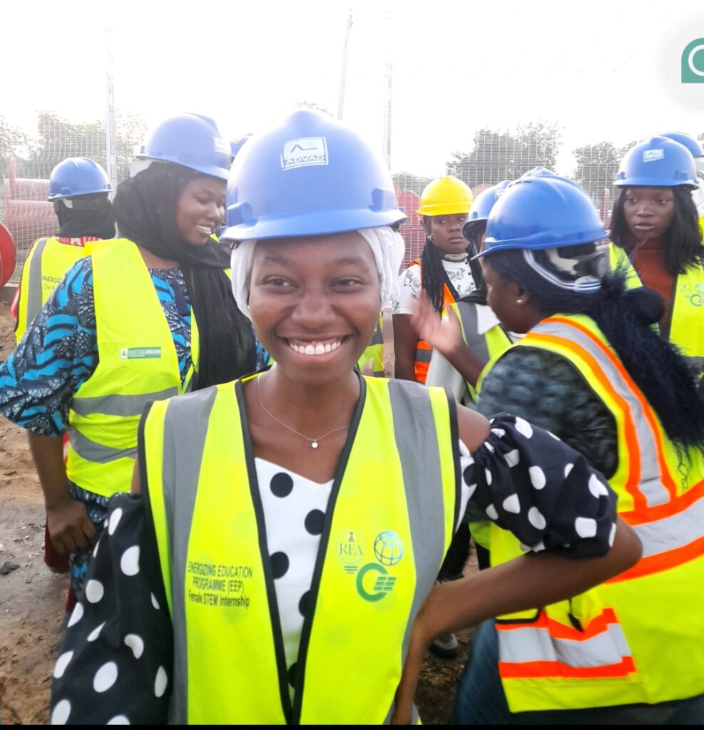 A smiling person in a hard hat and hi-vis vest with a group of similarly dressed people in the background.