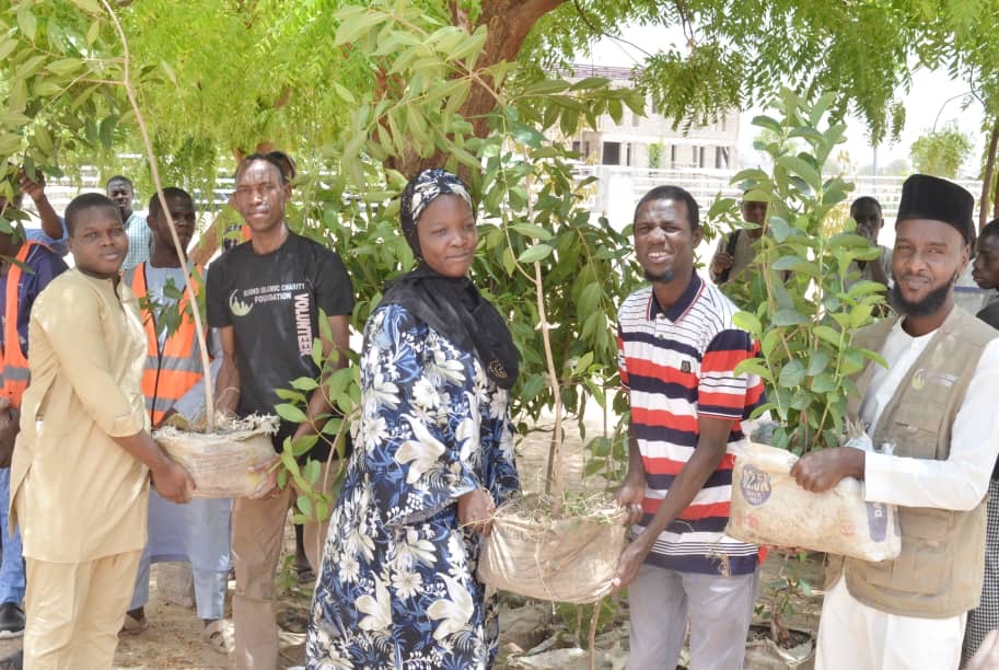 Group of people holding young trees ready for planting, smiling for a photo outdoors.