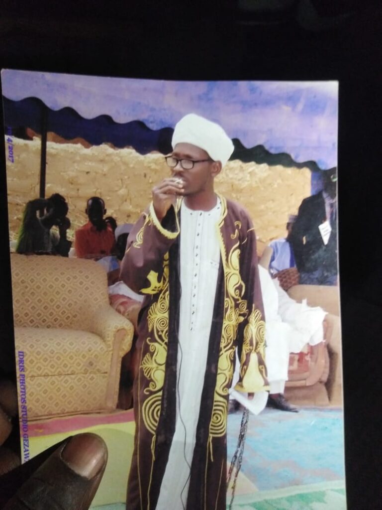 Man in traditional attire drinking water at an event with people in the background.