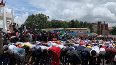 A crowd of people bowing down in prayer with some standing and waving a flag, possibly at a public gathering or demonstration.