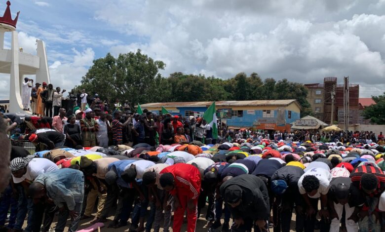 A crowd of people bowing down in prayer with some standing and waving a flag, possibly at a public gathering or demonstration.