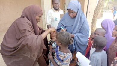 Health workers in hijabs administering care to children in an outdoor setting with onlookers.