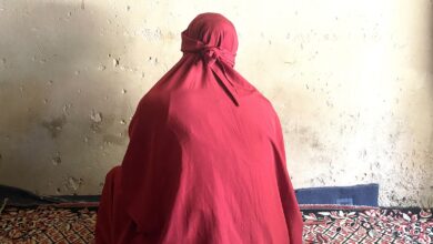 Person in red cloak sitting against a weathered wall on a patterned carpet.