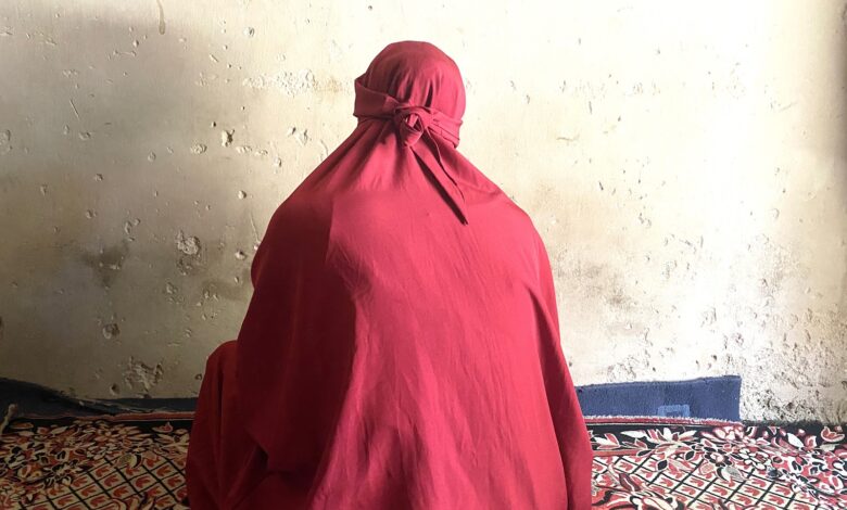 Person in red cloak sitting against a weathered wall on a patterned carpet.