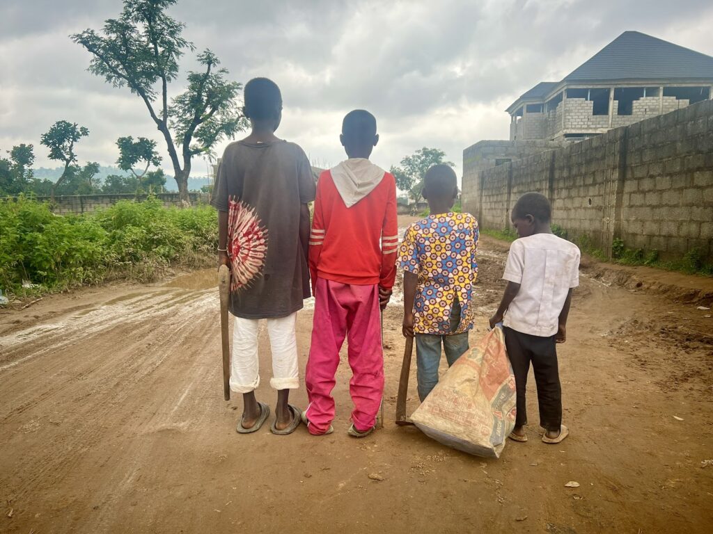 Four children from the back standing on a dirt road with building construction in the background.